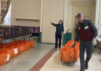 man pulling cart of grocery bags and woman directing placement of bags in church hall