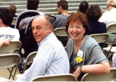 Charlie Utermohle and a woman sitting at an outdoor function, with heads turned back to look at the camera